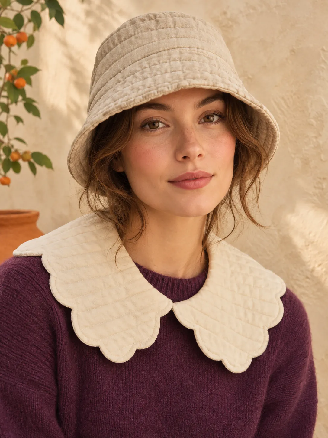 A woman wearing a cream scalloped quilted collar and an oat bucket hat